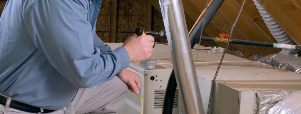 An HVAC technician is checking the ductwork and ventilation in an attic. 